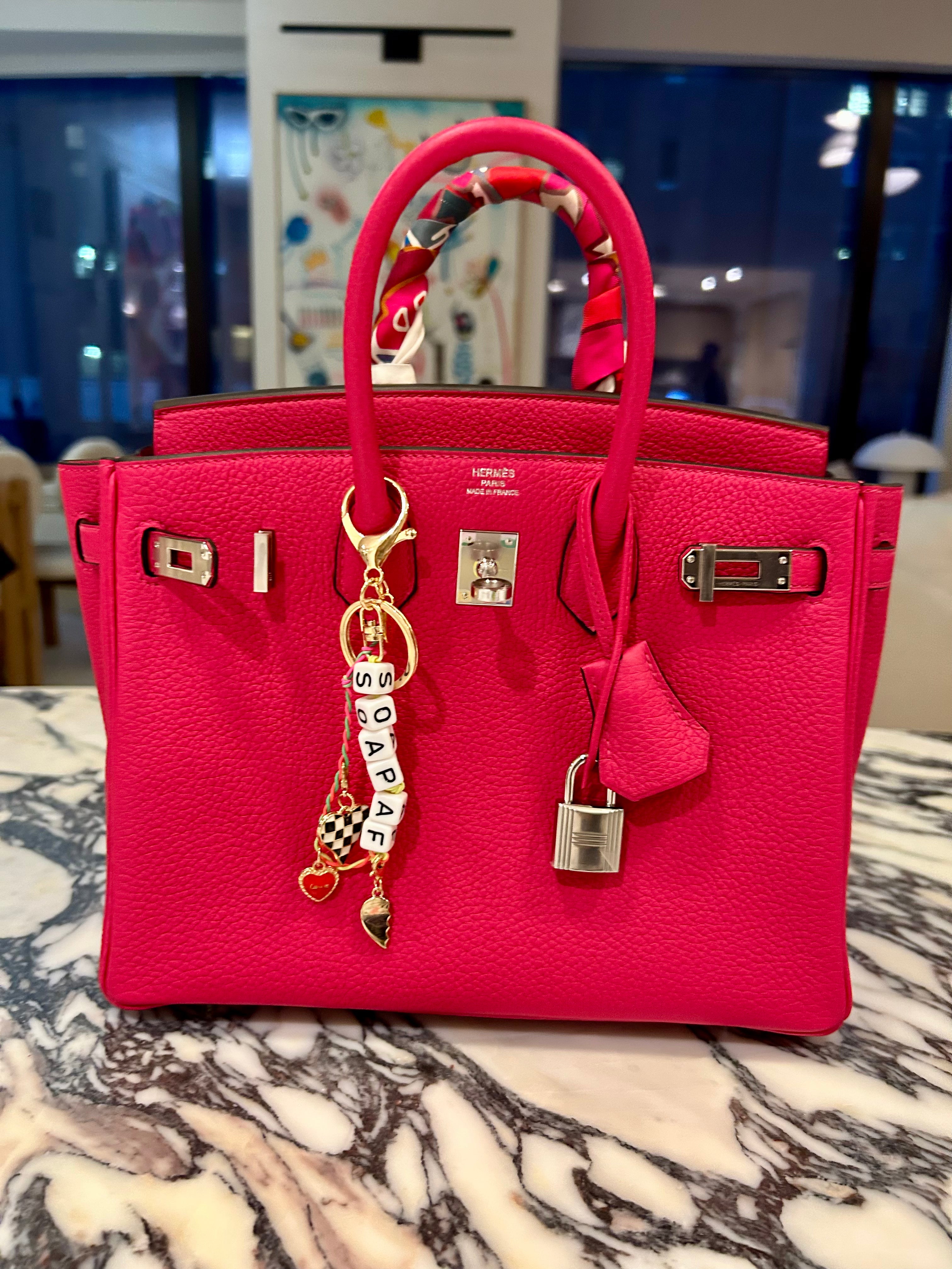 FORK & MELON SOAP AF beaded keychain charm on a bright pink designer Hermes handbag — black and white beaded detail with gold hardware and checkered heart accent, styled as a chic accessory.